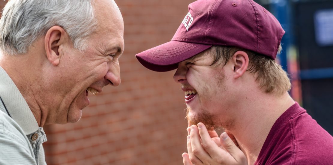 Grandfather laughing face to face with a his special needs grandson in a baseball uniform - Tisser Law Group Special Needs Trusts